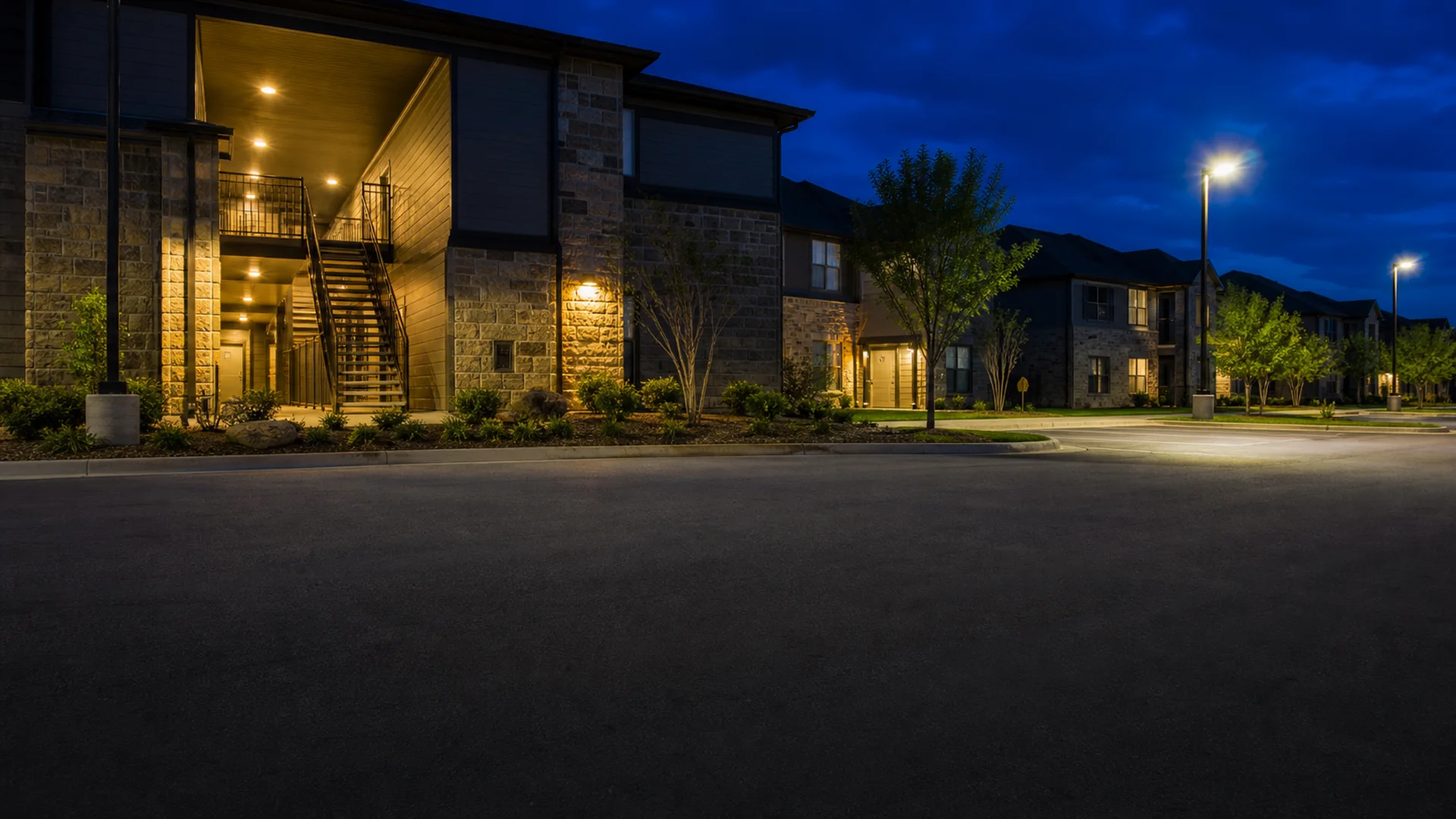 Evening exterior of a Texas apartment community with breezeway and parking lot lighting on