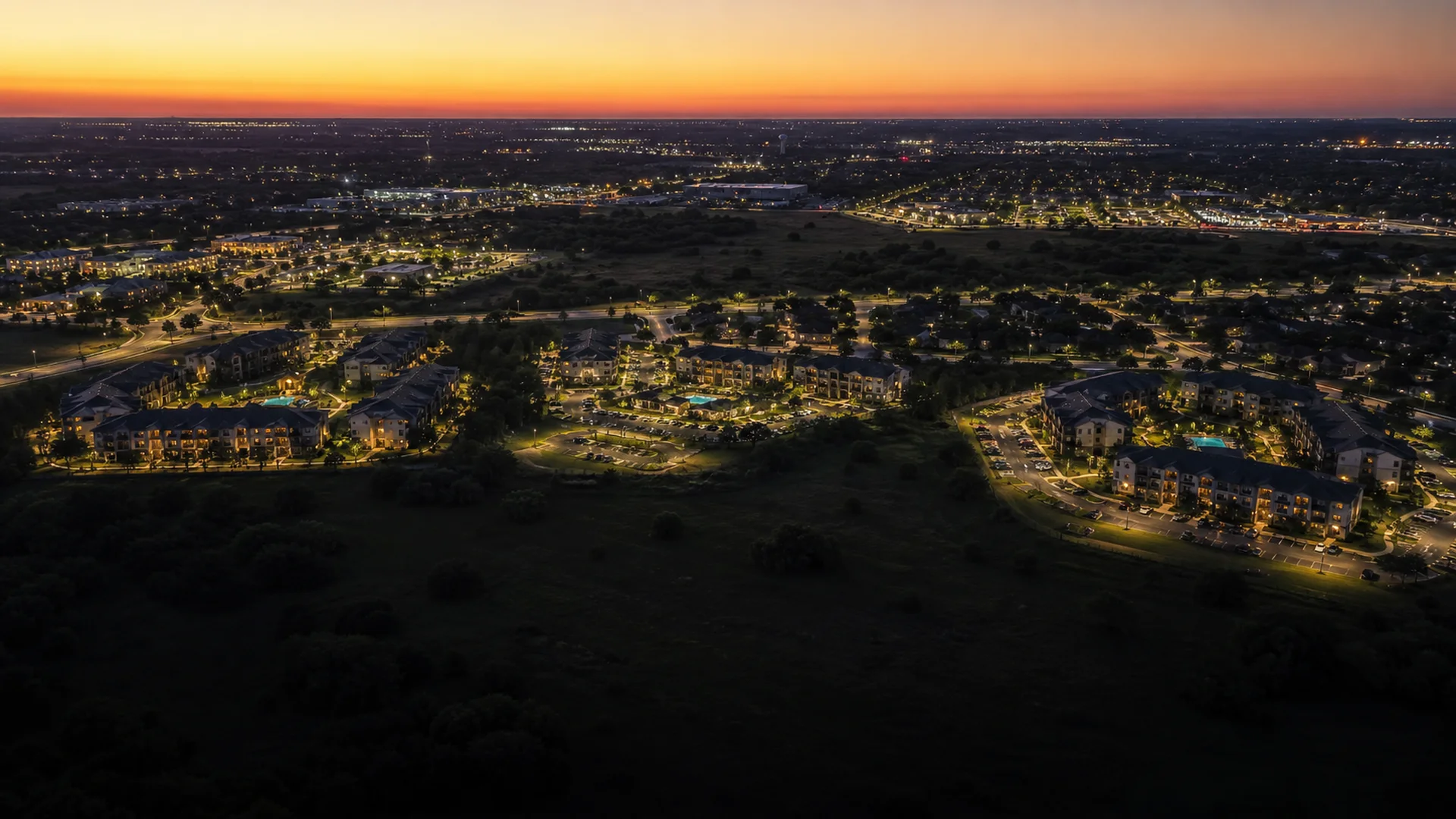 Aerial view at dusk of several Texas apartment communities across a suburban metro